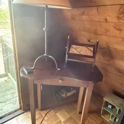 Sale Photo Thumbnail #241: Kidney-shaped wooden corner table featuring stud detail along the edge, topped with a tall forged metal table lamp and a small wooden swivel vanity mirror.
