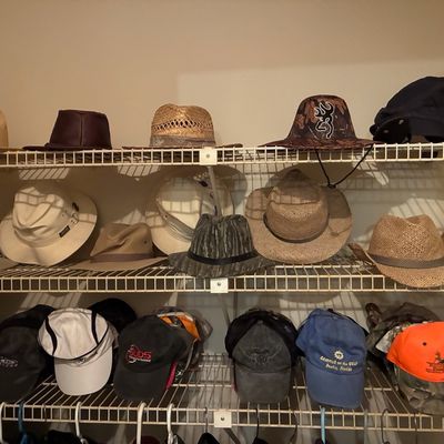 Sale Photo Thumbnail #203: Collection of men's hats stored on closet shelving, including straw hats, fedoras, camouflage sun hats, and various baseball caps.