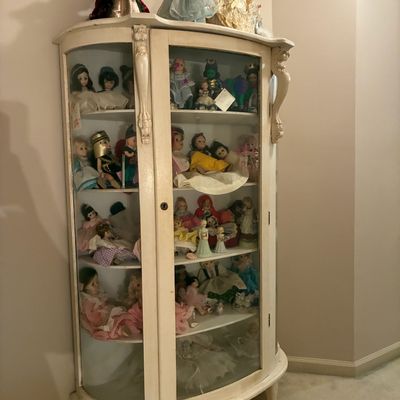 Sale Photo Thumbnail #201: Vintage white-painted curio display cabinet with rounded glass sides, filled with a large collection of porcelain and costume dolls.