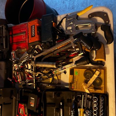 Sale Photo Thumbnail #20: Assortment of hand and power tools including a Ridgid tool box, staple gun, hole saw set, and socket set arranged on a folding table.