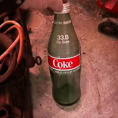 Sale Photo Thumbnail #102: Vintage 33.8 oz (1 liter) Coca-Cola green glass bottle with original screw cap, featuring printed 'Coke' logo and 'Return for deposit' marking.