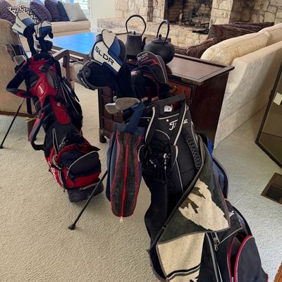 Sale Photo Thumbnail #5: Two stand golf bags filled with assorted clubs, including TaylorMade and Titleist brands, placed in a living room area.