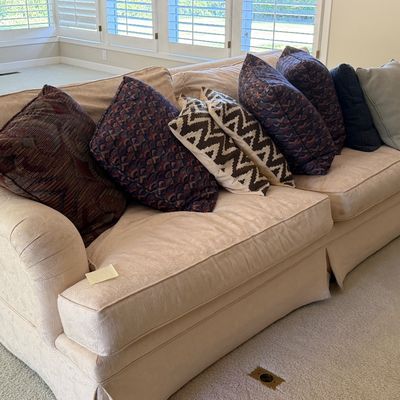 Sale Photo Thumbnail #9: Large beige skirted sofa featuring rolled arms and an assortment of patterned throw pillows.