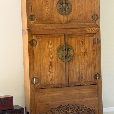 Sale Photo Thumbnail #4: Tall Asian-style wooden armoire cabinet featuring round brass hardware and a floral relief carving along the bottom apron.