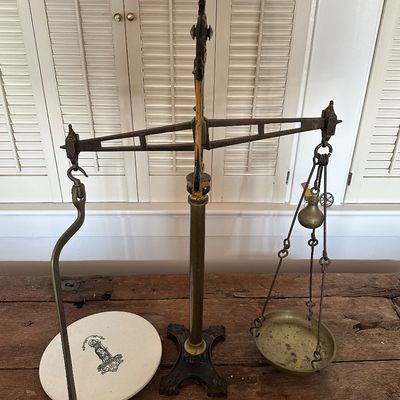 Sale Photo Thumbnail #53: Antique brass and cast iron balance scale featuring a ceramic plate on one side and a hanging brass pan on the other.