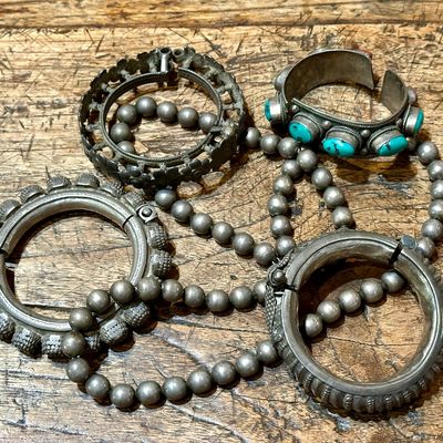 Sale Photo Thumbnail #93: Assortment of vintage silver jewelry including ornate tribal-style bangles, a beaded Navajo-style pearl strand, and a turquoise cabochon cuff bracelet.