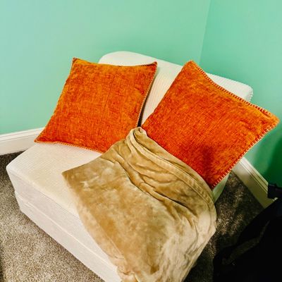 Sale Photo Thumbnail #74: Off-white upholstered armchair or ottoman module paired with two orange textured throw pillows and a beige fleece blanket.