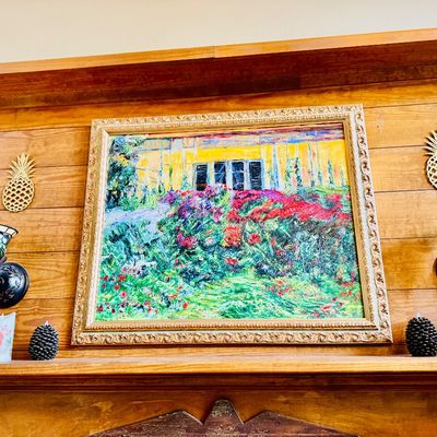 Impressionist-style garden scene painting framed in a gilded ornate frame, mounted on a wood-paneled wall above a mantel. Flanked by...
