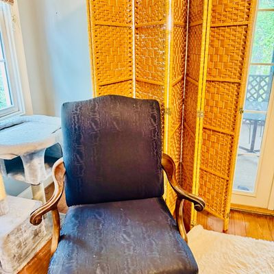 Vintage navy blue upholstered armchair with carved wooden arms and legs, set in front of a four-panel wicker folding room divider.