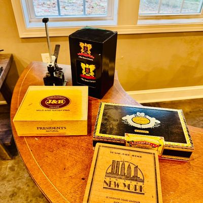 Sale Photo Thumbnail #30: Collection of vintage wooden and cardboard cigar boxes, including J&R Cigars, Partagas, and Te-Amo New York, arranged on a wooden table.