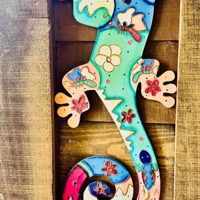 Sale Photo Thumbnail #21: Colorful hand-painted metal gecko wall art featuring whimsical floral and insect motifs, mounted on a wooden background.