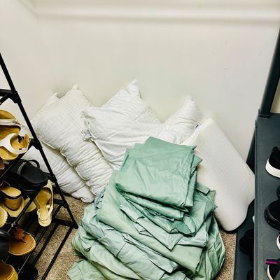 Sale Photo Thumbnail #98: Stack of folded sage green bed linens paired with an assortment of white sleeping and memory foam pillows on a closet floor.