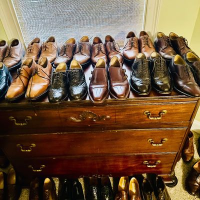 Sale Photo Thumbnail #88: Large collection of men's leather dress shoes, oxfords, and loafers displayed on and below a traditional wooden chest of drawers.