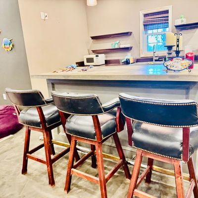 Sale Photo Thumbnail #57: Set of three vintage swivel bar stools with black leather upholstery, nailhead trim, and dark wood frames, positioned in front of a home bar counter.