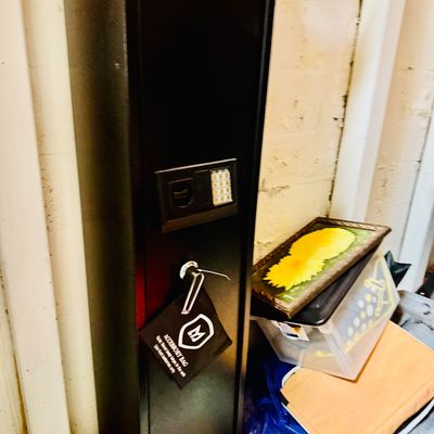 Sale Photo Thumbnail #44: Tall black steel gun safe with a digital keypad lock and turn handle, appearing in clean condition with attached accessory bag.
