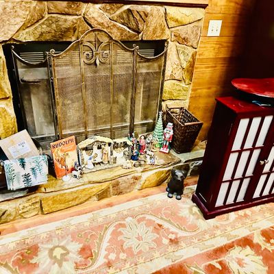 Sale Photo Thumbnail #91: Fireplace area decorated with a nativity set, vintage Christmas items, a brass fireplace screen, brass scuttle, and a nearby Asian-style cabinet with frosted glass doors.