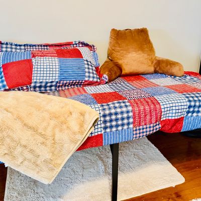 Twin platform bed frame styled with red, white, and blue patchwork bedding, a tan faux fur throw, and a plush backrest pillow.