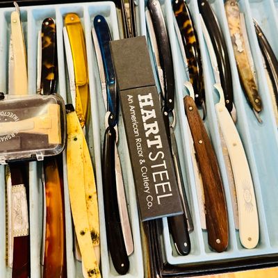 Collection of vintage straight razors arranged in slotted display cases, featuring various handle materials including celluloid, faux...