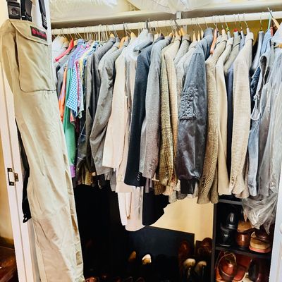 Sale Photo Thumbnail #49: Closet packed with men's clothing including suit jackets, sports coats, button-up shirts, and footwear, featuring a pair of tan fishing waders hanging from the door.