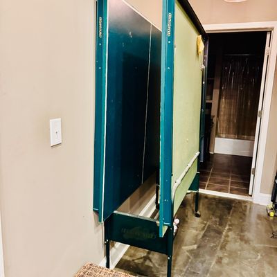 Sale Photo Thumbnail #43: Harvard folding ping pong table with a teal play surface and wheeled metal frame, shown stored vertically.