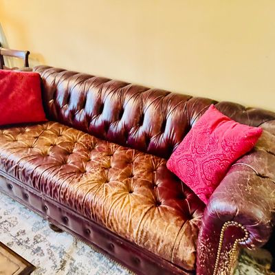 Sale Photo Thumbnail #50: Vintage Chesterfield tufted leather sofa in deep burgundy, featuring brass nailhead trim, rolled arms, and heavily patinated wear on the seat cushions.