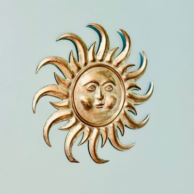 Sale Photo Thumbnail #73: Vintage gold-toned metal celestial sun face wall decor featuring wavy rays and a stylized embossed facial expression.