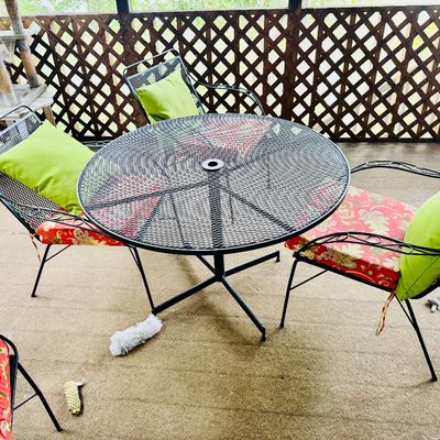 Sale Photo Thumbnail #23: Black wrought iron outdoor patio set including a round mesh-top table and matching armchair set, complete with red floral cushions and lime green throw pillows.