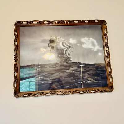 Framed nautical art print depicting a tall sailing ship on choppy waters, housed in an ornate carved wooden frame.