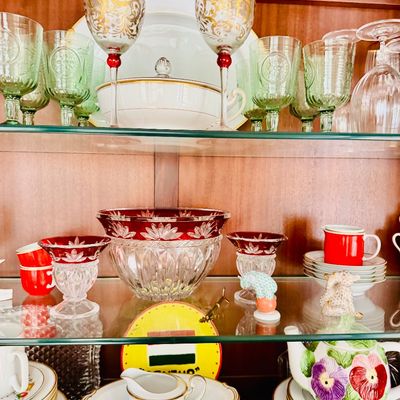 Sale Photo Thumbnail #79: Display cabinet filled with glassware and china, including ruby flash cut-to-clear bowls and wine glasses, green press-molded goblets, and gold-trimmed dinnerware.