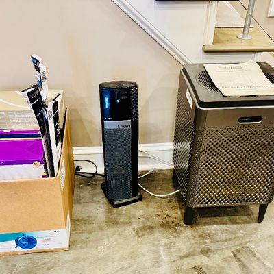 Sale Photo Thumbnail #39: Collection of household utility items, including a box filled with lighting supplies, a Lasko ceramic space heater, and a modern air purifier unit with its manual.