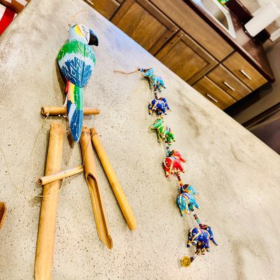 Sale Photo Thumbnail #59: Hand-painted parrot bamboo wind chime alongside a colorful Indian beaded elephant garland, resting on a countertop.