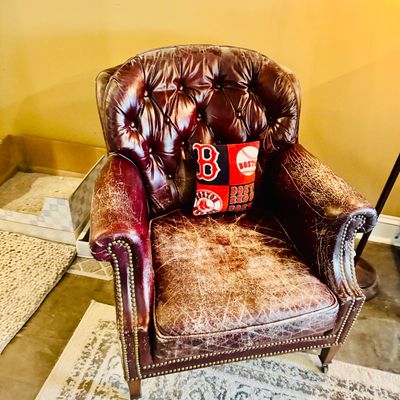 Sale Photo Thumbnail #55: Vintage tufted burgundy leather armchair featuring nailhead trim and front caster wheels, showing heavy surface wear and distressing.