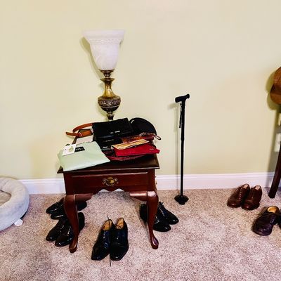 Sale Photo Thumbnail #83: Traditional wooden end table topped with assorted purses and a frosted glass shade table lamp, surrounded by pairs of dress shoes on the floor.