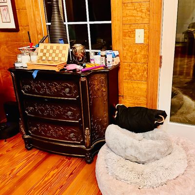 Sale Photo Thumbnail #92: Ornate dark wood chest of drawers with carved floral accents, topped with decor items, alongside a stack of plush round pet beds.
