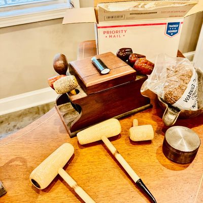 Sale Photo Thumbnail #31: Collection of vintage smoking pipes, including several corncob and briar wood pipes, displayed alongside a wooden pipe stand, tobacco, and smoking accessories.