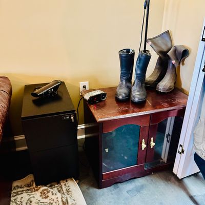 Sale Photo Thumbnail #46: Small wooden media cabinet alongside a modern black filing cabinet, featuring various pairs of boots and electronics on top.