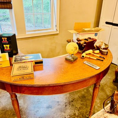 Sale Photo Thumbnail #29: Curved mahogany executive desk with inlaid edge detail, featuring various cigar boxes, tobacco pipes, and decorative items.