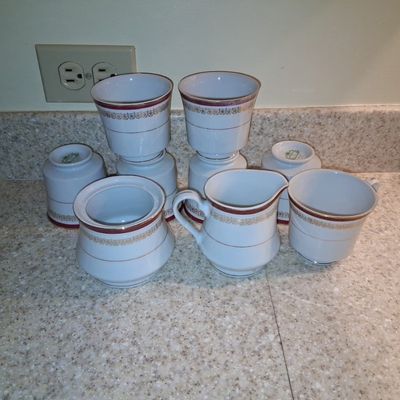 Sale Photo Thumbnail #109: Vintage white porcelain tea service set, featuring a sugar bowl, cream pitcher, and teacups with maroon and gold gilded accents.
