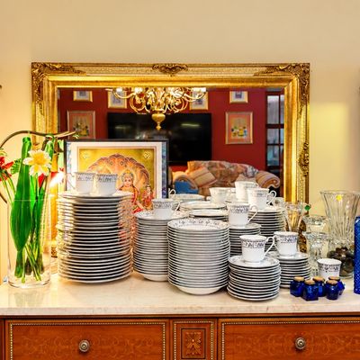Sale Photo Thumbnail #71: Large fine china dinnerware set displayed on a marble-top sideboard, framed by two ornate illuminated curio cabinets filled with cobalt blue and gilt glassware.
