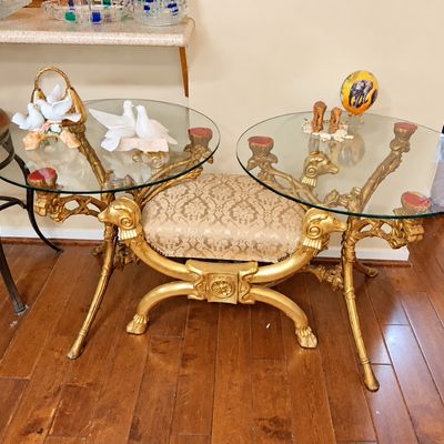 Sale Photo Thumbnail #101: Ornate gilt-finished dual glass-top side table featuring an integrated damask-upholstered bench seat, accompanied by decorative figurines.