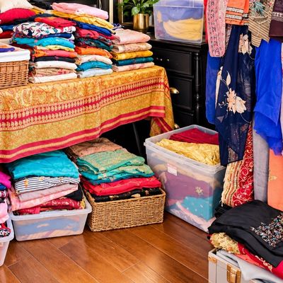 Sale Photo Thumbnail #60: Large collection of vibrant South Asian garments, including sarees, dupattas, and embroidered suits, organized in clear plastic storage bins, wicker baskets, and hanging racks.