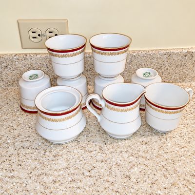 Sale Photo Thumbnail #91: Set of porcelain tea service pieces featuring a red and gold ornate band with gold trim, including cups, a creamer, and a sugar bowl.