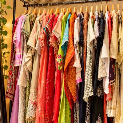 Sale Photo Thumbnail #62: Clothing rack filled with colourful South Asian garments, including embroidered kurtas and sarees, next to a full-length floor mirror.