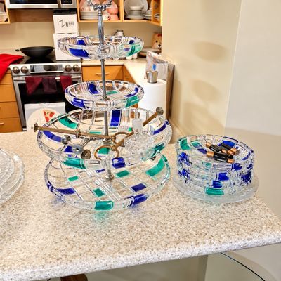 Sale Photo Thumbnail #99: A four-tier clear crystal serving stand with blue and teal grid accents, alongside a matching stack of small glass dishes on a kitchen counter.