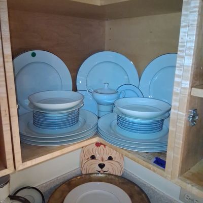 Sale Photo Thumbnail #110: A set of light blue ceramic dinnerware with platinum trim arranged inside a wooden corner cabinet.