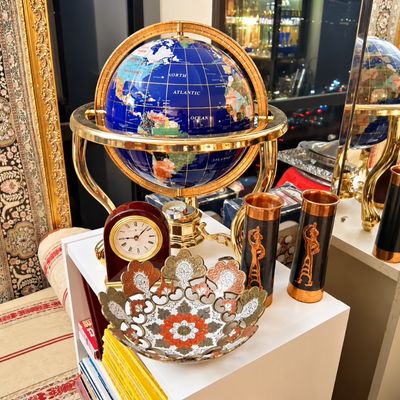 Sale Photo Thumbnail #97: Lapis lazuli gemstone desktop globe with brass stand, displayed alongside decorative brass vases, a small desk clock, and a floral reticulated bowl.
