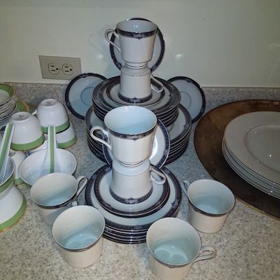 Sale Photo Thumbnail #108: Large collection of fine china tableware featuring stacked blue and white pattern teacups, saucers, and plates, alongside green-accented bowls and spoons.