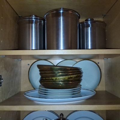 Sale Photo Thumbnail #106: Set of three stainless steel canisters and porcelain dishes displayed inside a wooden cabinet.