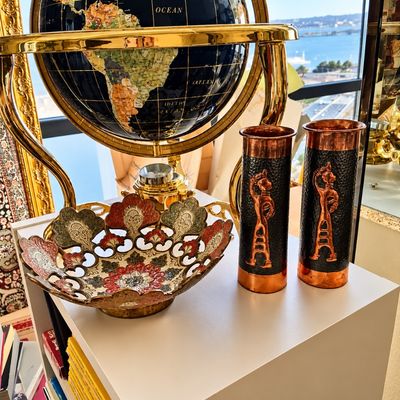 Sale Photo Thumbnail #78: Large black gemstone floor globe in a brass-finished gimbal stand, displayed alongside a hand-painted brass decorative bowl and a pair of embossed copper shell casing vases.