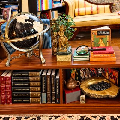 Sale Photo Thumbnail #70: Wooden coffee table with built-in bookshelves filled with books, a desk globe, art books, and decorative figurines, set between striped sofas on a patterned rug.